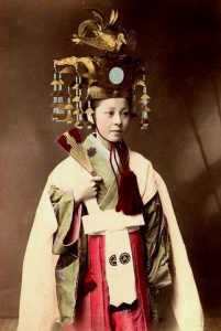 Old Miko with elaborate head dress, hand fan and attire