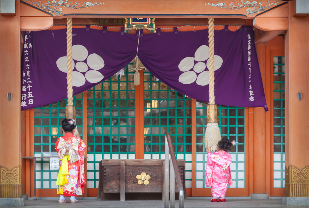 Two girls in kimono pray in front of the Shinto shrine building