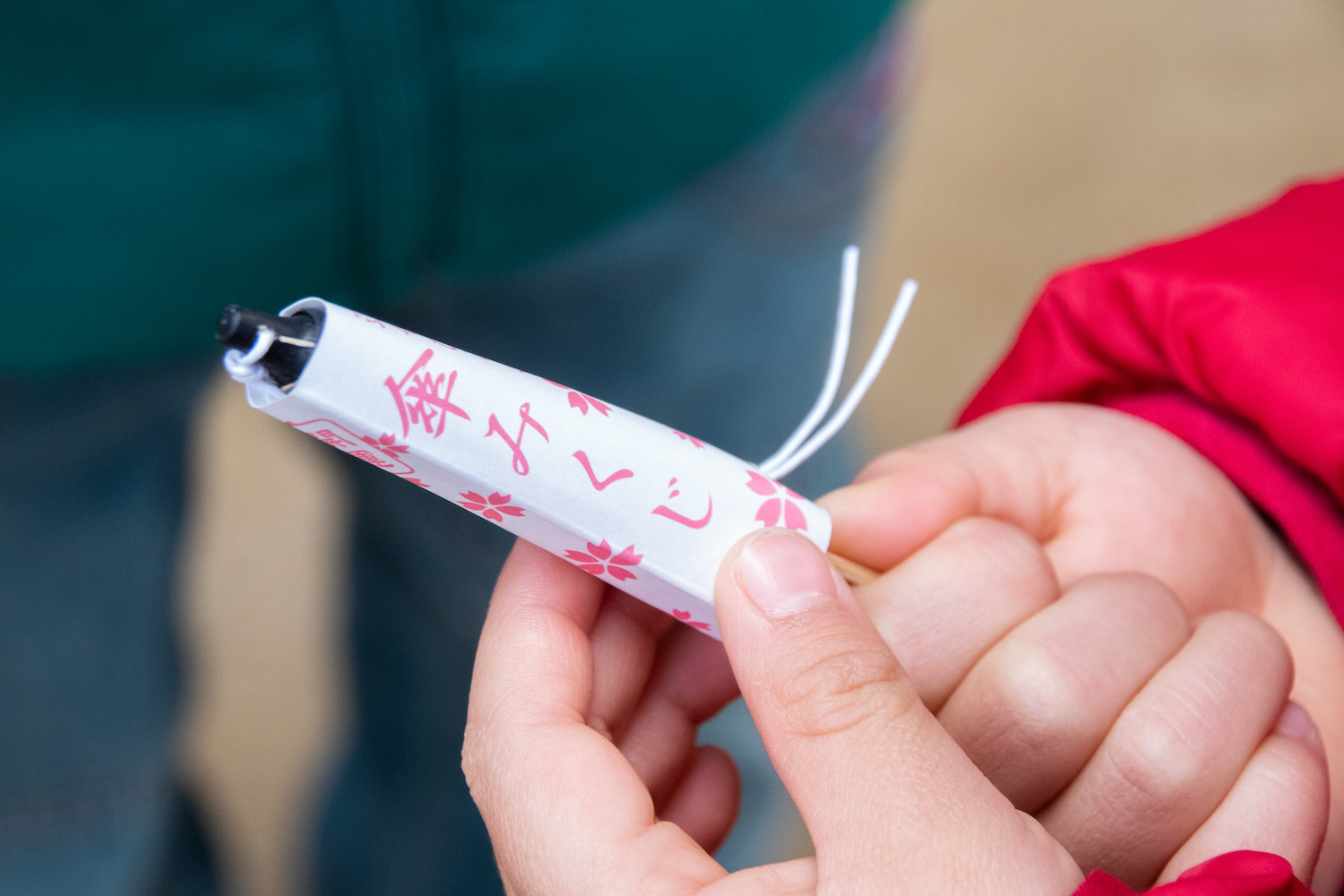 The hands of a child with Japanese umbrella-shaped fortune telling slips. Japanese characters are written on it. It says ' Kasa mikuji' which means ' the umbrella-shaped fortune telling'.