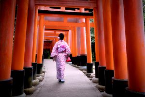 A woman in kimono walks under the torii gates of Fusimi Inari Shrine in Kyoto