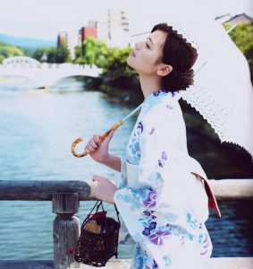 A woman in Yukata holding an umbrella and a purse