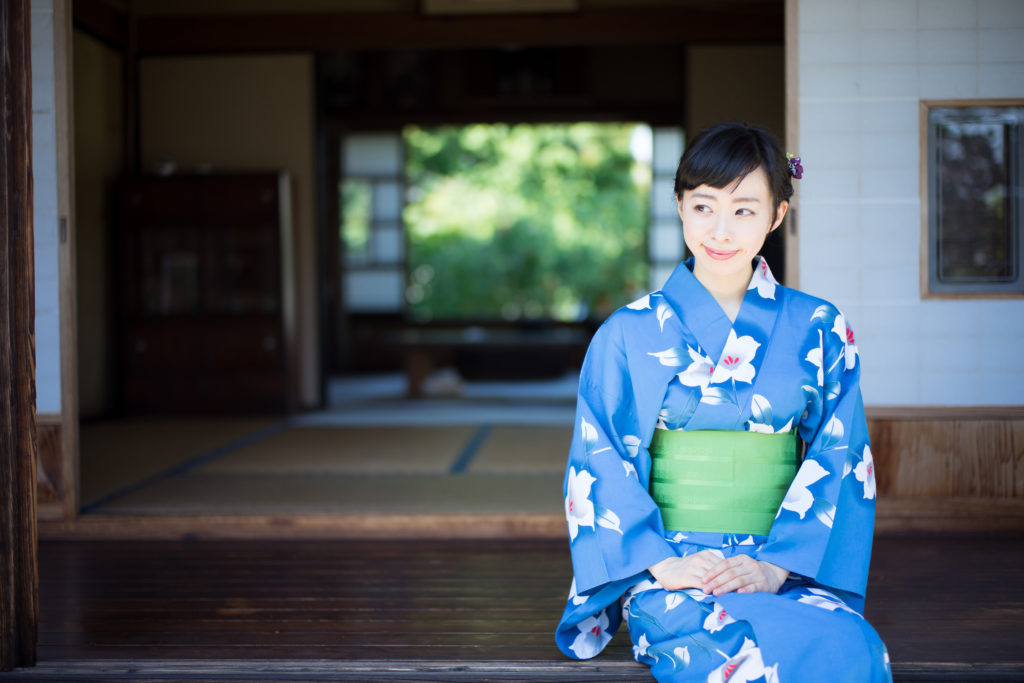 A woman in blue yukata, Japanese traditional casual summer dress, sits on the edge of veranda 