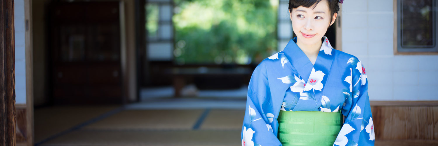 A woman in blue yukata, Japanese traditional casual summer dress, sits on the edge of veranda