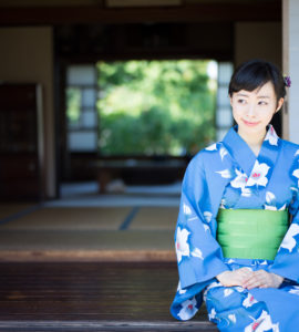 A woman in blue yukata, Japanese traditional casual summer dress, sits on the edge of veranda