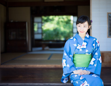 A woman in blue yukata, Japanese traditional casual summer dress, sits on the edge of veranda