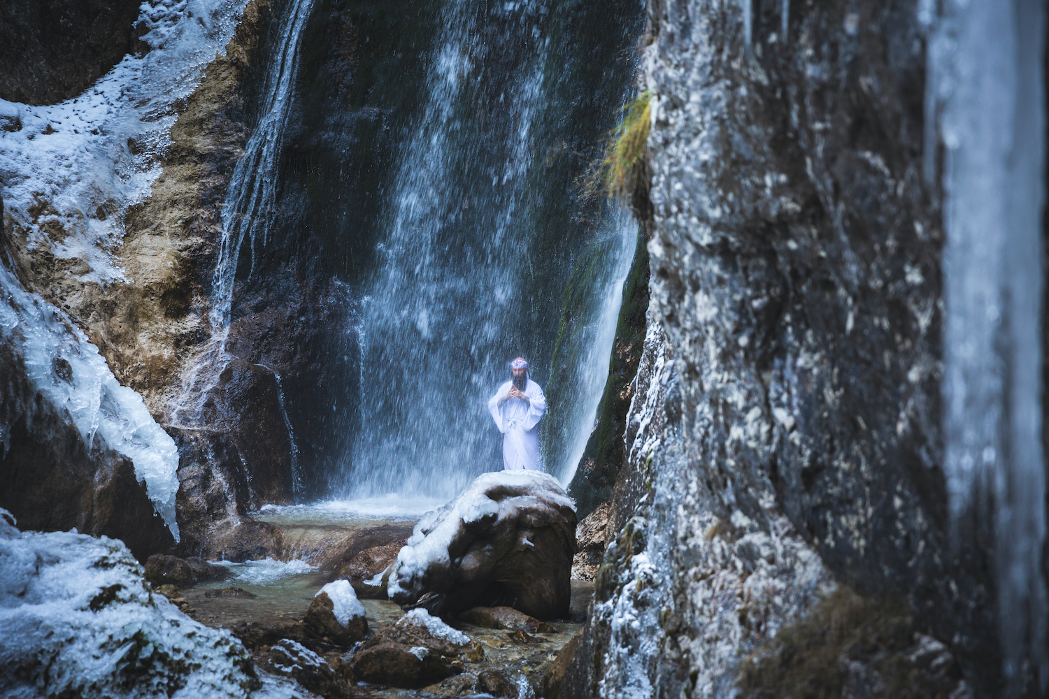 Man in traditional Japanese Shugendo outfit doing waterfall meditation in winter with ice and snow